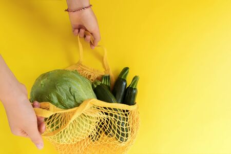 Top view of mesh shopping bag with organic eco green vegetables isolated on yellow background. Caring for the environment and zero waste conceptの写真素材