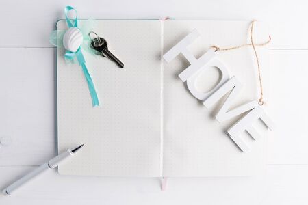 white notebook with home keys and a pen and a white wooden inscription Home, concept of planing a house buying, mortgage, debt or property loan, copy space, close upの写真素材