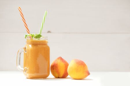 Healthy eating. Summer drink smoothies from fresh peach and vegan milk, decorated with mint leaves on a white wooden background, copy spaceの写真素材