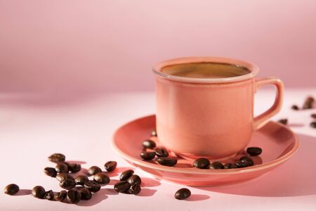 Coral colored cup with effuse coffee's beans with shadows on pastel rose background. Flat lay. Top view. Minimalism, Coffee concept. Pop art still life. Copy spaceの写真素材
