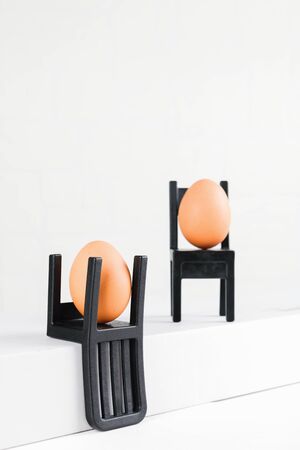Two eggs are sitting on black chairs. Business conference or consultation. Concept of business organisation, brainstorming, better choice. Minimale easter concept ideaの写真素材
