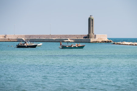 BARI, ITALY - JULY 11,2018, seascape with green lighthouse and a motor boat anchored with people taking sun, Apulia, Italyのeditorial素材