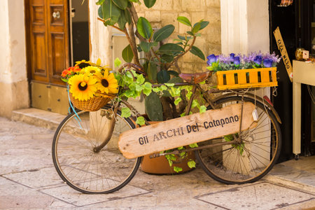BARI, ITALY - JULY 11, 2018, View of a narrow street in the center of Bari. An old bicycle decorated with flowers outside a shopのeditorial素材
