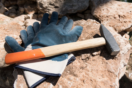 Close up of pair of protective gloves and masonry hammer on large stone boulder on construction site. Salento, Puglia, Italyのeditorial素材