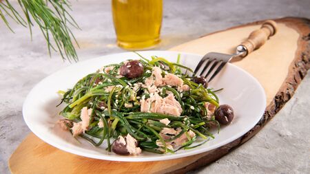 Light salad with agretti, a spring vegetable from Italy, tuna, black olives and olive oil for slimming and weight loss on a white plate on a gray background, tipical mediterranean dish, close upの写真素材