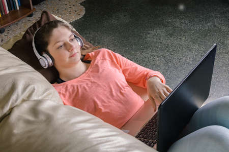 Smiling girl student wear wireless headphone comunicate or study online, happy young woman learn language listen lecture watch webinar, look at laptop, distant education and e-learningの写真素材