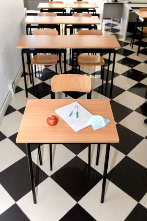 Desk with an apple, medical mask and a copybook in an empty classroom, new normal, back to school...