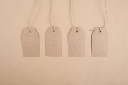 Four tags of recycled kraft paper for packaging hanging from a rope on a kraft paper background. Space for textの写真素材