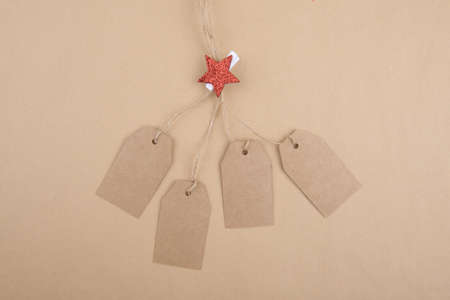 Four tags of recycled kraft paper hanging from a rope decorated with a clothespin with a red...