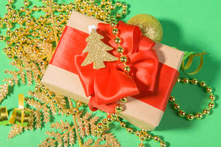 Christmas background with gift box with red ribbon bow on festive golden decoration on a green...