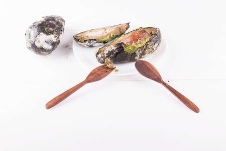 Creative concept of stop wasting food, don't waste food in supermarket and at home. Sliced rotten avocado on a plate with knife and fork, copy spaceの写真素材