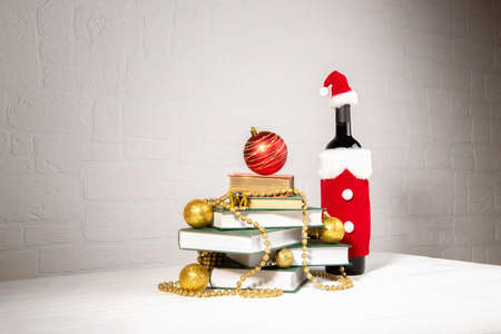 Christmas tree made of books with chistmas balls decoration on table with bottle of wine wearing of Santa Claus red hat and wear on brick wall background, Happy New Year and Merry Chrismasの写真素材