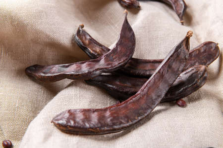 Dry carob pods on a linen nakpin background. Organic healthy ingredient for vegan vegetarian food and drinks, close upの写真素材
