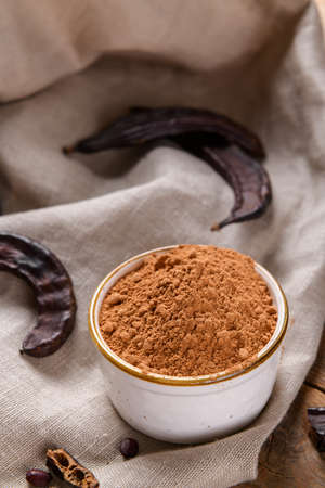Dry carob pods and carob powder on linen napkin, natural background
