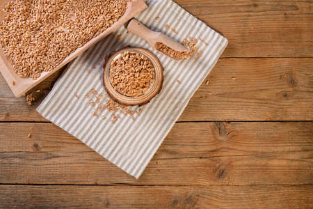 Wholegrain uncooked raw spelt farro in a bowl on napkin with wooden scoop on wooden background, top...