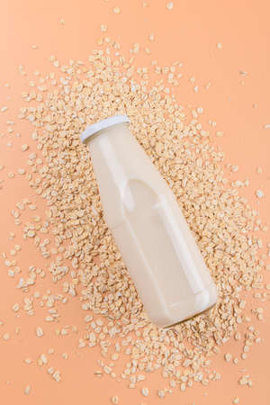 Vegan non dairy alternative milk. Oat milk in a bottle on the oat flake on pastel peach color...