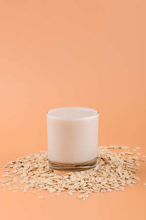 Vegan non dairy alternative milk. Oat milk in a glass on the oat flake on pastel peach color background, copy spaceの写真素材