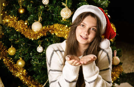 a young woman wearing santa hat smiling on camera, teenager girl dreaming and making a wish on a Christmas festive background, selective focusの写真素材