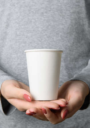 Female hands holding blank empty take away paper cup on neutral grey backgroundの写真素材