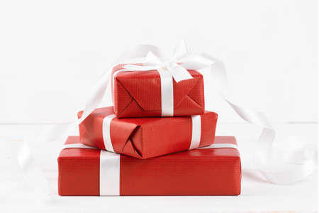 Close up of three red gifts boxes with white ribbon on white wooden background, copy space. Christmas or Valentine Day presentの写真素材