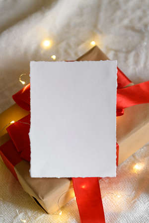 Christmas winter empty 5x7 card mockup on a kraft gift on a knitted beige background with light garland, design element for invitation, thank you or greeting card. Christmas cozy backgroundの写真素材