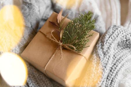 Kraft gift box with fresh fir branch decoration on knitted gray and beige sweater and garland for special event, top view. Cozy Christmas still life, birthday or new year, valentines day giftの写真素材