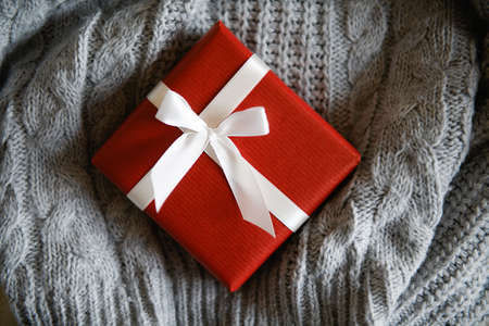 Red kraft gift box with white ribbon on knitted gray sweater, present for special event, top view. Cozy Christmas still life, birthday or new year, valentines day giftの写真素材