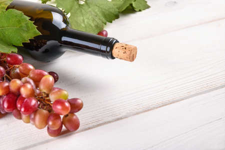 Close up of red wine bottle with grapes and green grapes leaves on white wooden table background with copy spaceの写真素材