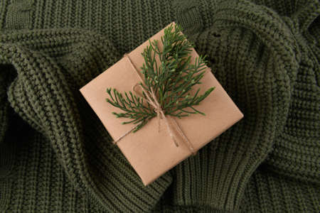 kraft gift box with fir decoration on knitted green sweater, the sleeves of the sweater are like hands holding a gift. Cozy Christmas still life, birthday or new year, valentines day giftの写真素材