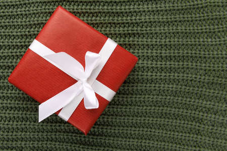 Red kraft gift box with white ribbon on knitted green sweate, top view. Cozy Christmas still life, birthday or new year, valentines day gift, copy spaceの写真素材