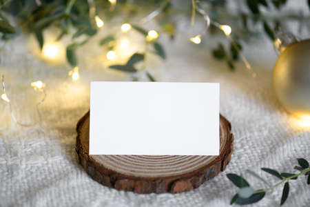 Christmas empty stationery card mockup with eucaliptus leaves and light garland on knitted beige cozy winter background, design element for invitation, thank you or greeting card, business card, rsvpの写真素材