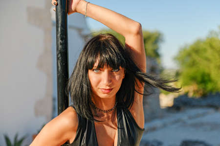 Strong Woman making a pose on a pole. Pole dancer training outside in summer, sport for everyone.