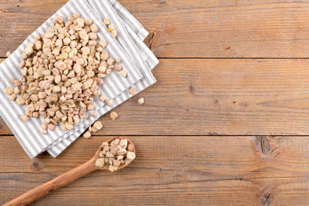 Dry raw cicerchia or indian pea on cotton napkin and in wooden spoon on natural wooden background,...
