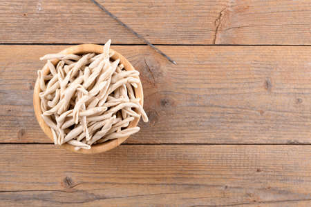 Whole grain wheat raw apulian pasta Pizzarieddi or maccaruni in a bowl on wooden table. Fresh maccheroni typical dish of Puglia Salento Italy. Italian homemade pasta background, close up, top viewの写真素材