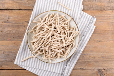 Whole grain wheat raw apulian pasta Pizzarieddi or maccaruni on a plate on wooden table. Fresh maccheroni typical dish of Puglia Salento Italy. Italian homemade pasta background, close up, top viewの写真素材