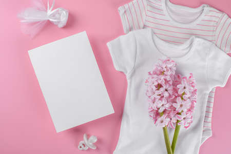 Baby shower invitation 5x7 card mockup with baby accessories girl bodysuit, nipple or baby's dummy, gift box and confetti and pink hyacinth flowers with copy space on pink pastel color backgroundの写真素材