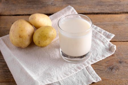 Vegan potato milk in a glass and potato tubers on brown wooden background. close up. Plant based alternative milk replacer and lactose free, Trendy healthy vegetarian and vegan drink conceptの写真素材