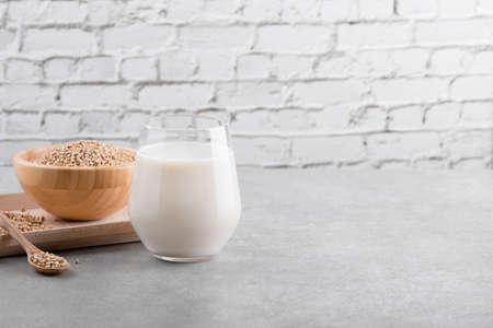 Vegan non diary buckwheat milk in glass with wooden bowl with buckwheat groats on a gray stone table. Vegan buckwheat drink is plant based alternative milk . Veggies healthy milk product, copy spaceの写真素材