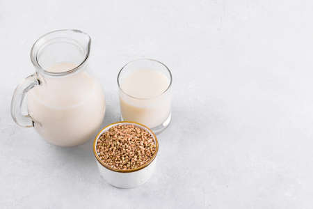 Vegan non diary buckwheat milk in jug and glass with buckwheat groats a bowl on a white stone table. Vegan buckwheat drink is plant based alternative milk . Veggies healthy milk product in pitcherの写真素材