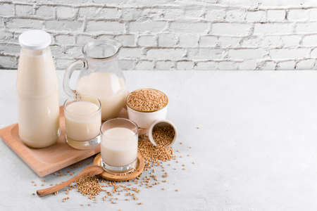 Vegan non diary buckwheat milk in bottle, in jug and glasses with buckwheat groats in a bowl on white stone table. Vegan buckwheat drink is plant based alternative milk. Veggies healthy milk productの写真素材