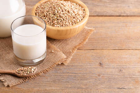 Vegan non diary buckwheat milk in glass with buckwheat groats and wooden spoon on a wooden backgroundの写真素材