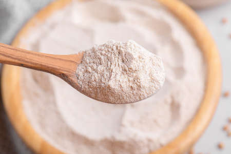 Buckwheat flour in a wooden bowl with wooden spoon, close up, top view, selective focus. Alternative flour, gluten free flour, healthy nutritionの写真素材