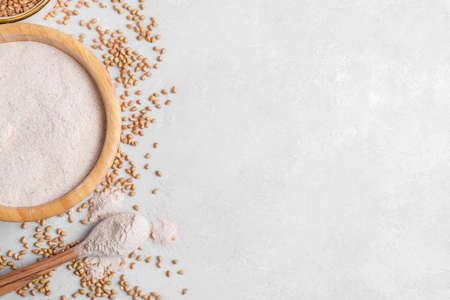 Buckwheat flour in a wooden bowl with wooden spoon and raw green buckwheat grain in a bowl on light gray stone background, close up, top view. Alternative flour, gluten free flour, healthy nutritionの写真素材