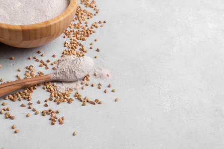 Buckwheat flour in wooden spoon and bowl with raw green buckwheat grain on light gray stone background, close up, top view. Alternative flour, gluten free flour, healthy nutritionの写真素材
