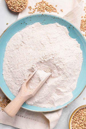 Buckwheat flour in a blu ceramic plate and in wooden scoop, raw green buckwheat grain on a bowl and napkin on light gray table background, top view. Alternative gluten free flour, healthy eatingの写真素材