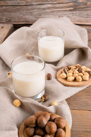 Vegan non diary hazelnut milk in glass with whole hazelnuts on a linen napkin on a rustic wooden background. Lactose free hazelnut drink is plant based alternative milk. Healthy milk product, close upの写真素材