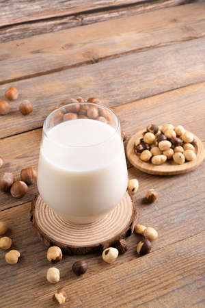 Vegan non diary hazelnut milk in glass with whole hazelnuts on a linen napkin on a rustic wooden background. Lactose free hazelnut drink is plant based alternative milk. Healthy milk product, close upの写真素材