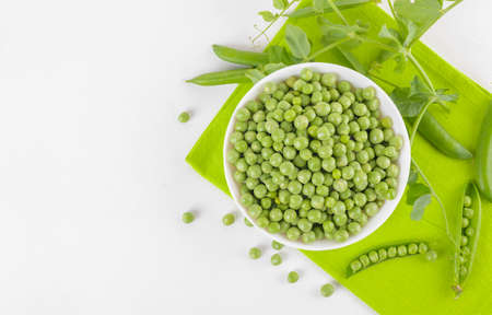 Fresh organic raw green peas in a bowl with peas plants leaves on a napkin on white background. Healthy eating, vegan and vegetarian legume food, raw food and detox super food, bean protein, top viewの写真素材