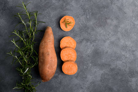 Raw whole orange sweet potato and slices of batatas with fresh rosemary on gray concrete background, top view, copy space, flat layの写真素材