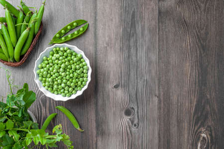 Fresh organic raw green peas in a bowl with peas plants leaves on dark wooden table background, bean protein, aboveの写真素材